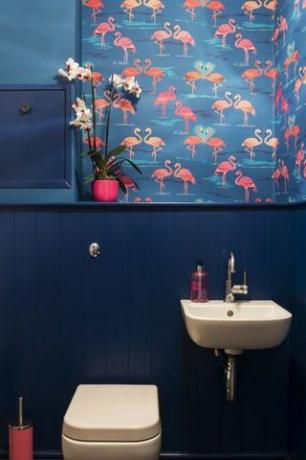 Cuarto de baño con papel pintado flamingo, lavabo blanco y paredes azules.