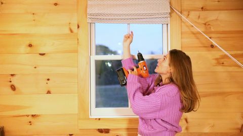 mujer sosteniendo taladro delante de la ventana