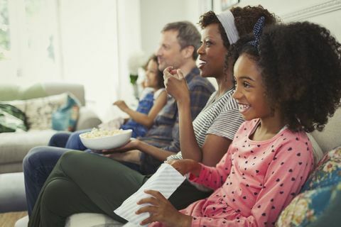 Joven familia multiétnica viendo películas y comiendo palomitas en el sofá