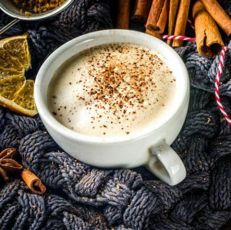 Bebida caliente dulce de otoño, ron chai con mantequilla, pastel de calabaza o café con leche con especias de calabaza Fondo de otoño acogedor con taza de café con leche tradicional, especias y suéter viejo, sobre fondo de madera rústica