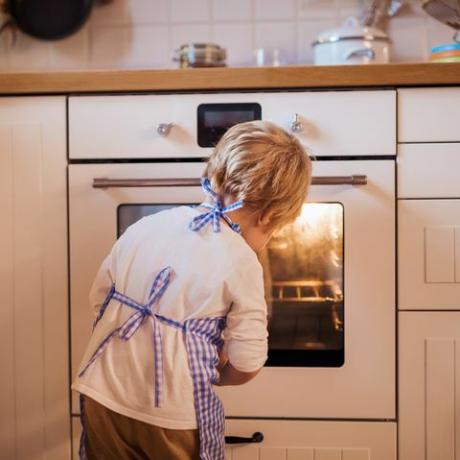 Niño pequeño mirando en el horno en el interior, hornear