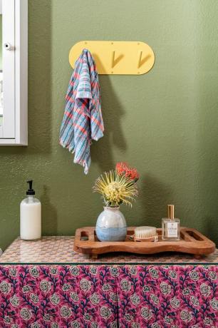 baño con pared verde y ganchos amarillos para toallas