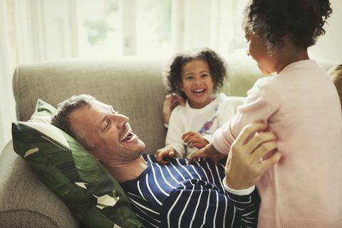 Padre e hijas cosquillas y riendo en el sofá