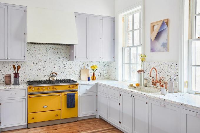 Los gabinetes pintados en calluna suave y sutil de Farrow Ball complementan la gama Lacanche de color amarillo cítrico y las encimeras de terrazo arcoíris en esta cocina de Manhattan diseñada por Penélope August.