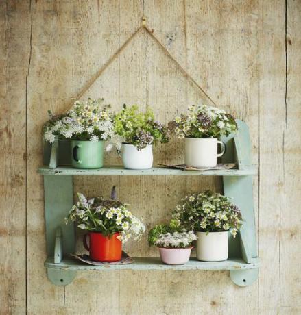 Estante colgante con tazas de esmalte que contienen flores.