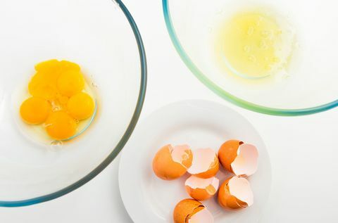 Yema de huevo y clara de huevo en un recipiente de vidrio separado. Cáscara de huevo y huevo en plato blanco.