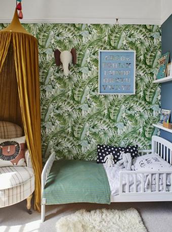 dormitorio infantil con papel pintado con estampado de palmeras tropicales y dosel amarillo