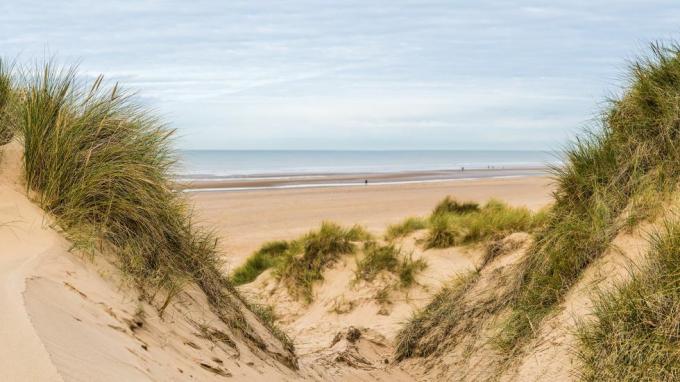 un panorama de múltiples imágenes capturado entre dos picos en las dunas de arena mirando hacia abajo a la gente caminando por la playa formby cerca de liverpool