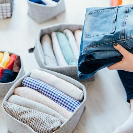 mujer doblando ropa en el dormitorio, organizando la ropa en cajas y cestas concepto de estilo de vida minimalista y sistema de plegado de camisetas japonesas método konmari