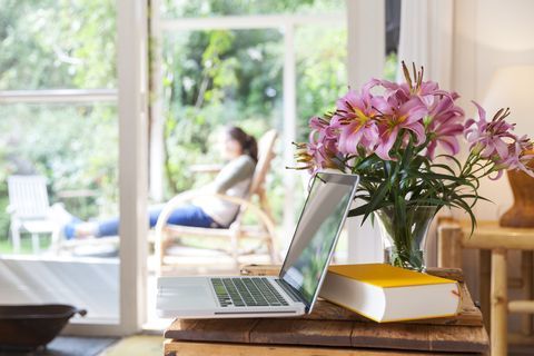 Flor decorada sala de estar con libro y computadora portátil. Mujer relajante afuera en una terraza