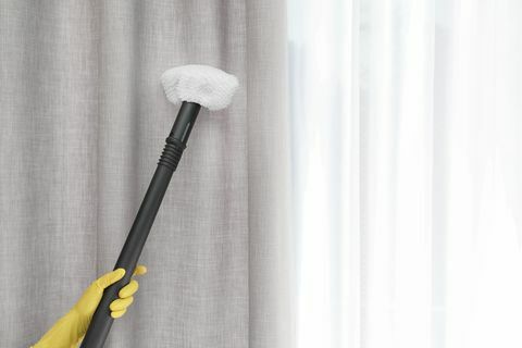 Conserje quitando el polvo de la cortina con limpiador a vapor en interiores, primer plano