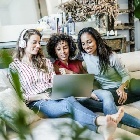 Tres mujeres felices con laptop sentada en el sofá