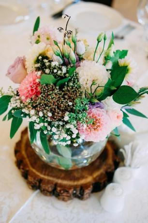 Decoración de flores de mesa de boda. Florero de vidrio con número de mesa para invitados con vegetación, rosas, lisianthus y otras flores.