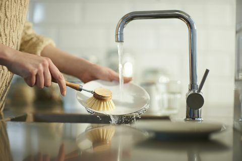 una mujer usa un cepillo sin plástico para limpiar platos en un fregadero de cocina, cerrar