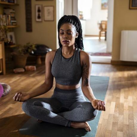 Mujer negra sentada en una habitación soleada meditando en posición de loto