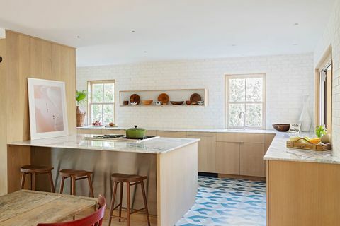 cocina con gabinetes de madera, encimeras de mármol, azulejos azules, blancos y grises, taburetes de madera