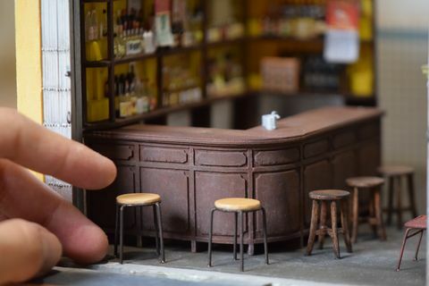 Primer plano de una réplica en miniatura de un bar, con taburetes y una mano humana para escalar