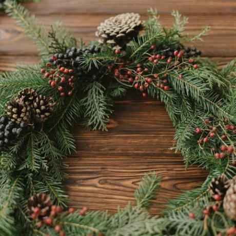 Corona de Navidad moderna con frutos rojos, ramas verdes, conos de pino, decoraciones de árboles naturales sobre fondo rústico Corona de Navidad rústica en mesa de madera Feliz Navidad