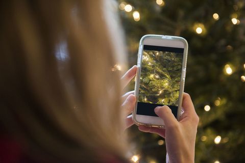 Mujer fotografiando árboles de Navidad con teléfono móvil