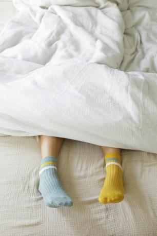 Mujer vistiendo calcetines azules y amarillos en la cama.