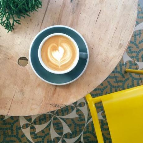 Taza de café con espuma de corazón en taza verde azulado sobre mesa de madera