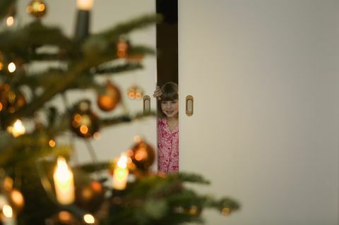 Chica en pijama mirando por la puerta en el árbol de Navidad