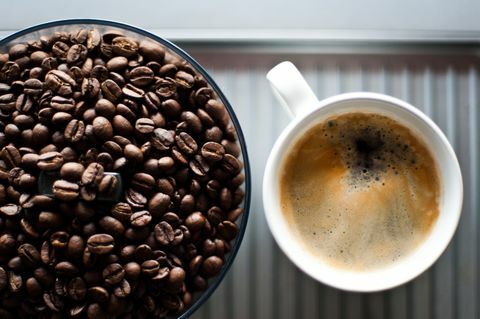 Granos de café frescos en un molinillo, además de una taza de café negro recién hecho