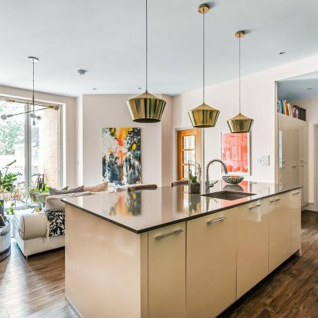 una isla de cocina moderna con iluminación colgante en el centro de una sala de estar de planta abierta en un apartamento contemporáneo